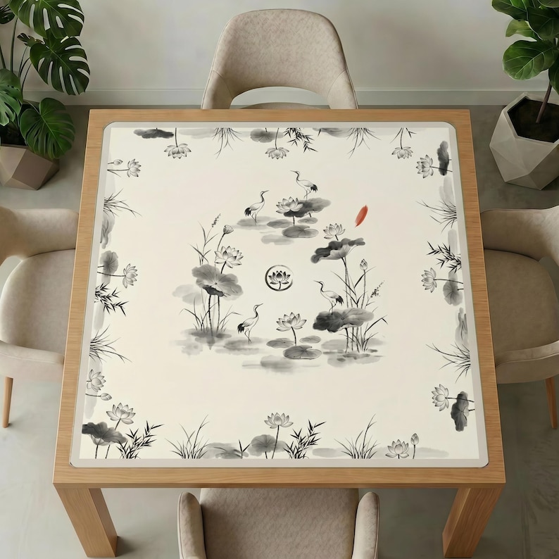 Wooden dining table with beige chairs and plants, topped with the ink crane and lotus mahjong table mat, showing the full black‑and‑white brush painting design.