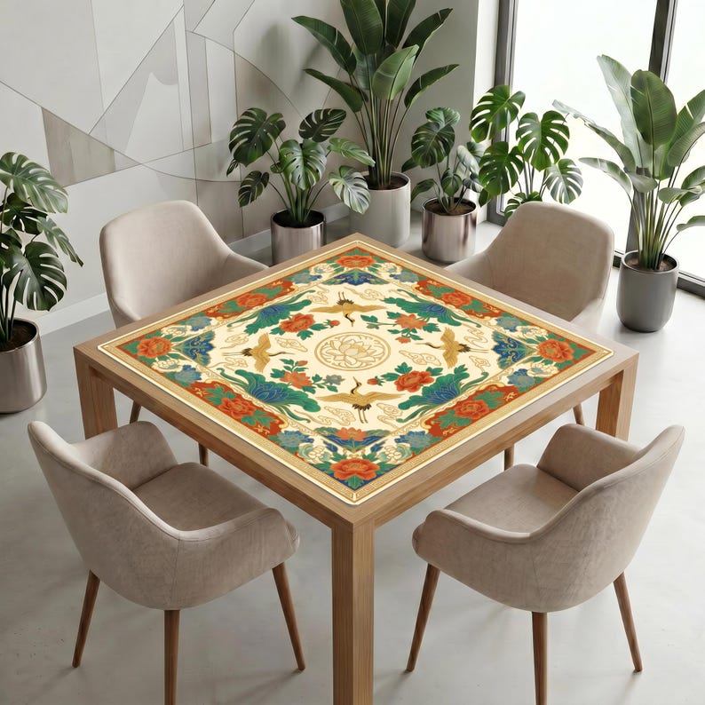 Modern dining space with many green plants and neutral chairs, featuring a wooden table covered by the colorful crane lotus mahjong table mat as a decorative centerpiece.