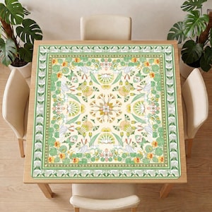 Green crane and lotus mahjong table mat covering a square wooden dining table, surrounded by light chairs and large potted plants.