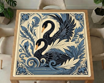 May include: A square table cover featuring a detailed illustration of two black swans with orange beaks, surrounded by blue and cream-colored stylized foliage and floral motifs. The design is framed by a decorative border with corner flower accents.