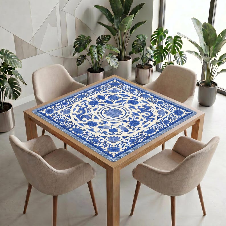Blue and white dragon lotus mahjong mat displayed on a square table in a bright modern room, styled with chairs and tall potted plants.