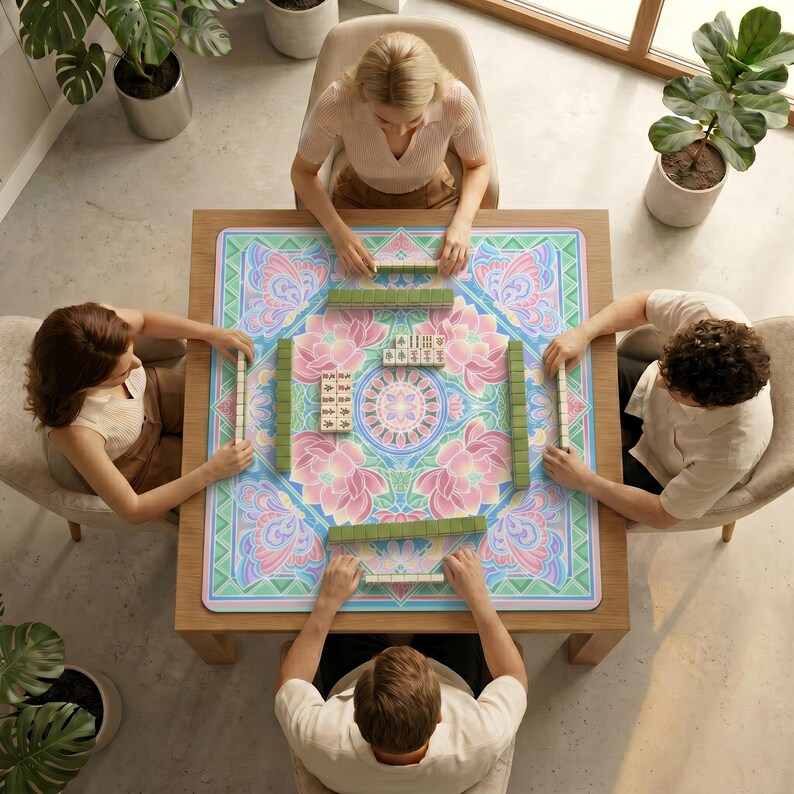 Top‑down view of four people sitting around a table covered with the pastel lotus mahjong table mat, preparing to play mahjong.