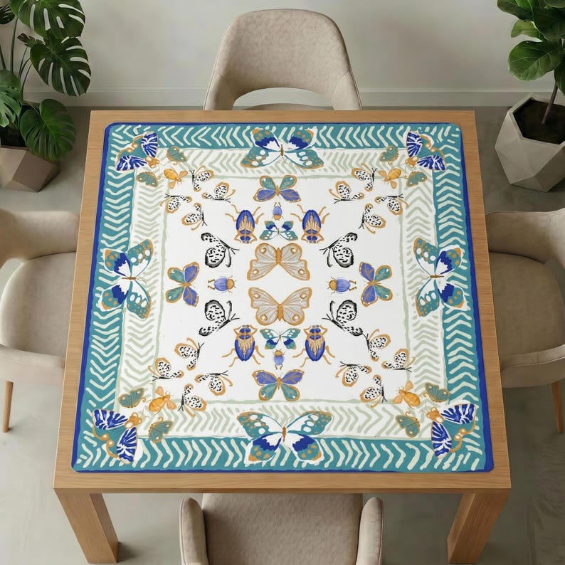 Wooden dining table with beige chairs and plants, topped with the teal border butterfly mahjong table mat covering the whole tabletop.