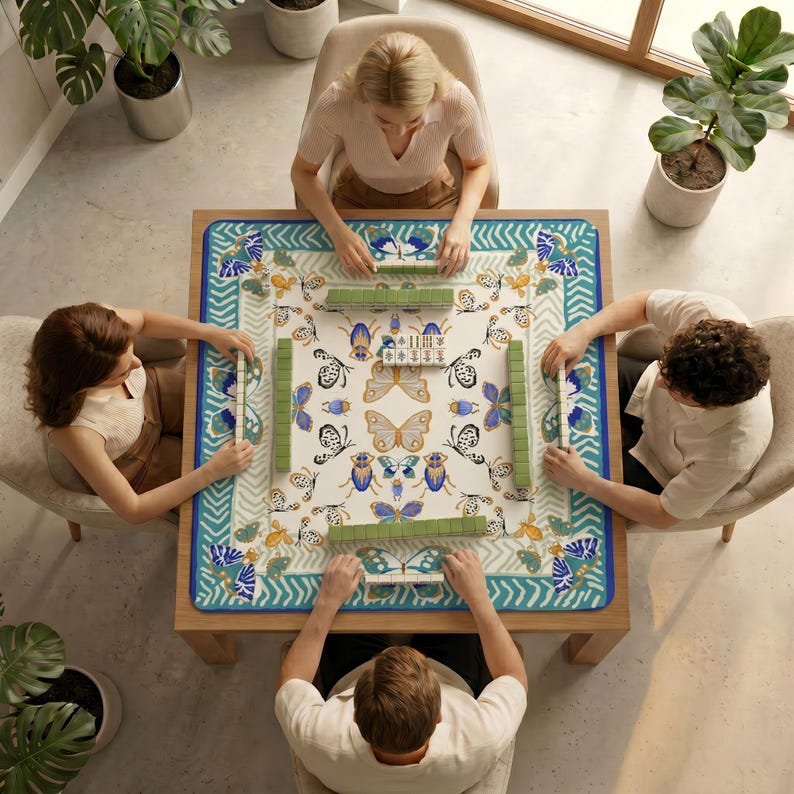 Top‑down view of four people sitting around a table covered with the butterfly insect mahjong table mat, preparing to play mahjong.