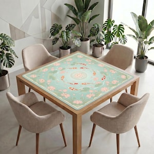 Koi and lotus mahjong mat displayed on a square table in a modern room, surrounded by soft chairs and tall potted plants near large windows.