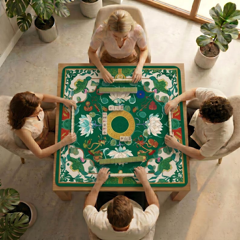 Overhead scene of four players seated around a table using the green lotus mahjong mat, emphasizing the full table setup and decorative border.