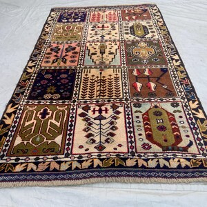 Pu&ograve; includere: Un tappeto rettangolare caratterizzato da una griglia di dodici pannelli distinti, ognuno contenente motivi geometrici e floreali unici nei toni del blu navy, crema, verde oliva, marrone e rosa, rifinito con un bordo blu scuro e frange.