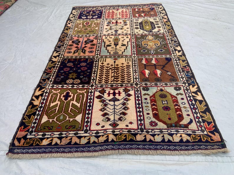 Pu&ograve; includere: Un tappeto rettangolare caratterizzato da una griglia di dodici pannelli distinti, ognuno contenente motivi geometrici e floreali unici nei toni del blu navy, crema, verde oliva, marrone e rosa, rifinito con un bordo blu scuro e frange.