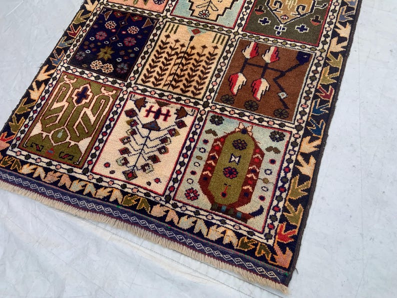 Pu&ograve; includere: Un tappeto rettangolare caratterizzato da una griglia di pannelli distinti, ognuno contenente motivi geometrici e floreali unici nei toni del blu navy, verde oliva, marrone, crema e rosso. Il tappeto &egrave; rifinito con un bordo decorativo e frange.