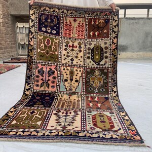 Pu&ograve; includere: Un tappeto rettangolare caratterizzato da una griglia di dodici pannelli distinti, ognuno dei quali mostra motivi geometrici e floreali unici in tonalit&agrave; blu navy, verde oliva, rosa, marrone e crema. Il tappeto &egrave; rifinito con frange alle estremit&agrave;.