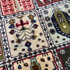 Pu&ograve; includere: Un tappeto rettangolare caratterizzato da una griglia di pannelli distinti, ognuno contenente intricati motivi geometrici e floreali in tonalit&agrave; verde oliva, blu scuro, crema, rosso e marrone, con un bordo scuro che separa ogni sezione.