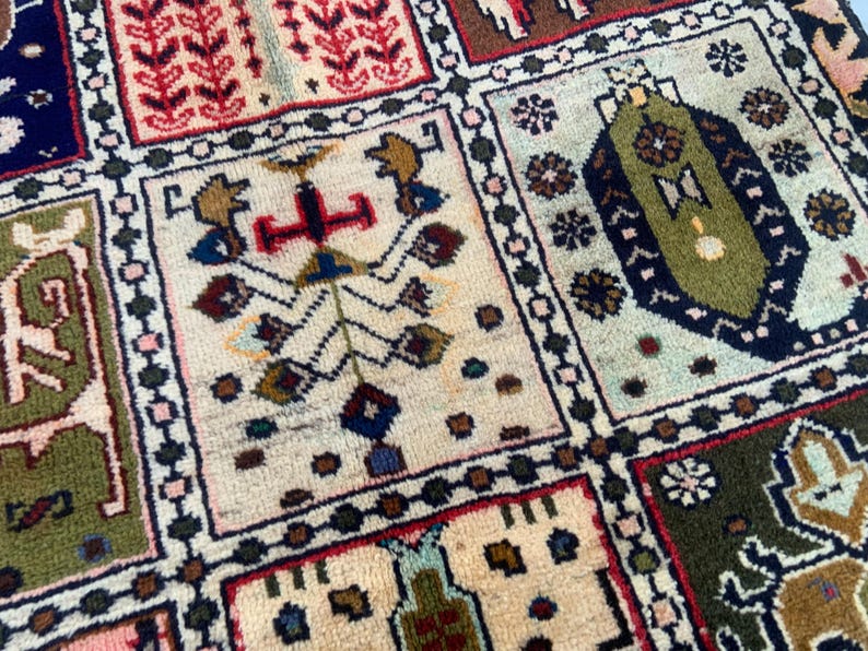 Pu&ograve; includere: Un tappeto rettangolare caratterizzato da una griglia di pannelli distinti, ognuno contenente intricati motivi geometrici e floreali in tonalit&agrave; verde oliva, blu scuro, crema, rosso e marrone, con un bordo scuro che separa ogni sezione.