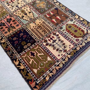Pu&ograve; includere: Un tappeto rettangolare caratterizzato da una griglia di pannelli multicolori con svariati motivi geometrici e floreali nei toni del verde oliva, blu navy, crema, rosa e marrone, rifinito con un bordo blu scuro e frange corte alle estremit&agrave;.