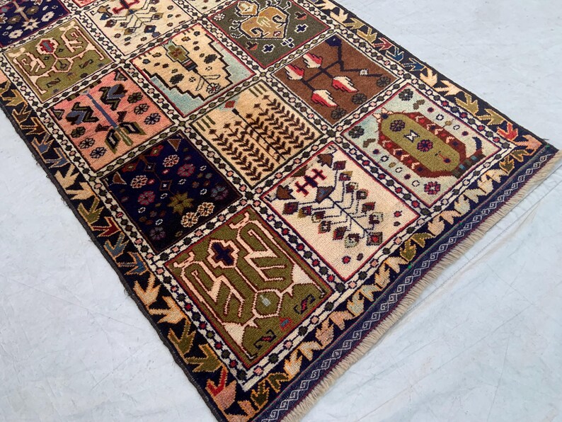 Pu&ograve; includere: Un tappeto rettangolare caratterizzato da una griglia di pannelli multicolori con svariati motivi geometrici e floreali nei toni del verde oliva, blu navy, crema, rosa e marrone, rifinito con un bordo blu scuro e frange corte alle estremit&agrave;.