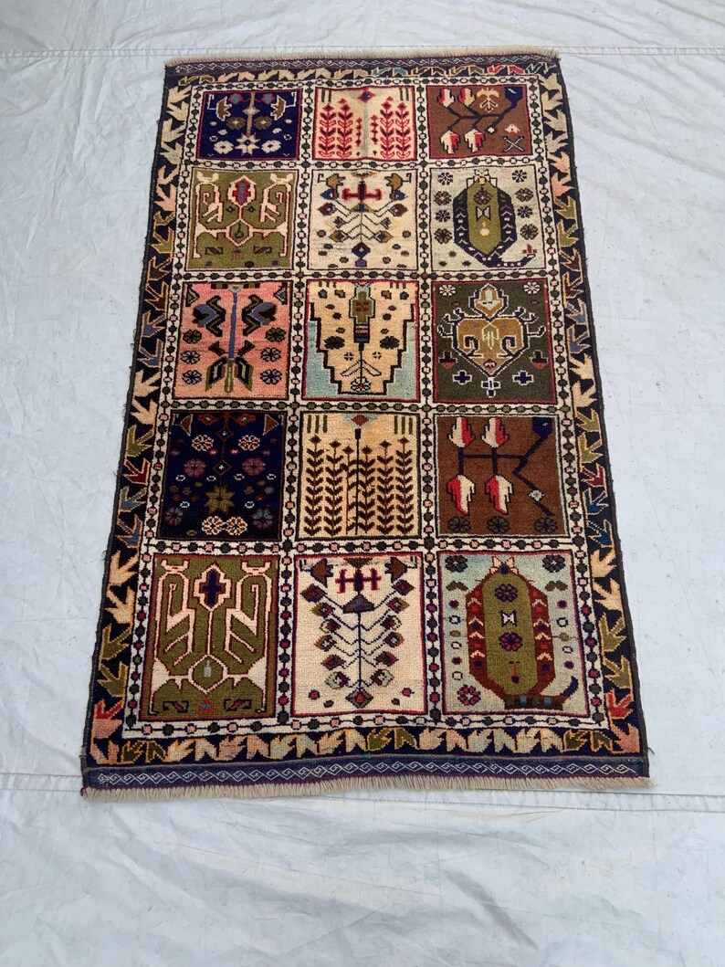 Pu&ograve; includere: Un tappeto rettangolare caratterizzato da una griglia di dodici pannelli distinti, ognuno dei quali mostra motivi geometrici e floreali unici nei toni del blu navy, verde oliva, terracotta, rosa e crema, racchiusi da un bordo scuro decorato.