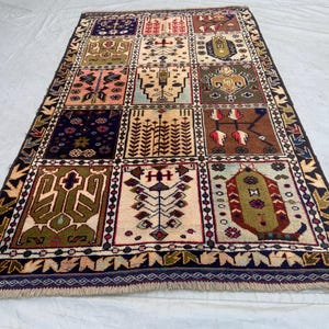 Pu&ograve; includere: Un tappeto rettangolare caratterizzato da una griglia di dodici pannelli distinti, ognuno contenente motivi geometrici e floreali unici nei toni del blu navy, crema, verde oliva, marrone e rosa, rifinito con un bordo blu scuro e frange.