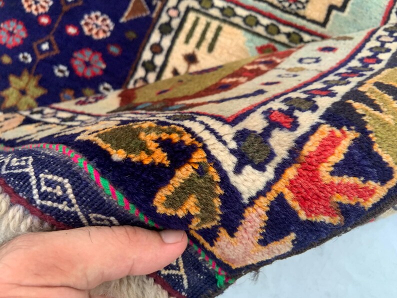 Pu&ograve; includere: Un tappeto in lana annodato a mano con un campo blu profondo e intricati motivi floreali e geometrici in rosso, arancione, verde e crema. Il bordo presenta un design complesso con motivi ripetitivi, un pelo spesso e una trama densa.