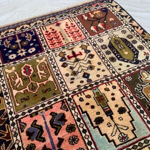 Pu&ograve; includere: Un tappeto rettangolare caratterizzato da una griglia di pannelli distinti, ognuno contenente motivi geometrici e floreali unici nei toni del blu navy, verde oliva, crema, rosa e marrone. Il tappeto presenta un bordo scuro con un motivo a frecce.