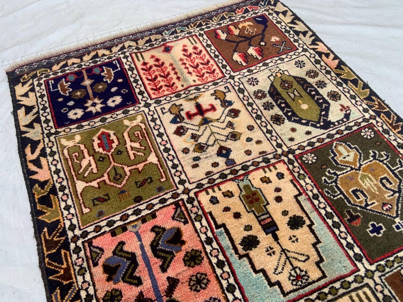 Pu&ograve; includere: Un tappeto rettangolare caratterizzato da una griglia di pannelli distinti, ognuno contenente motivi geometrici e floreali unici nei toni del blu navy, verde oliva, crema, rosa e marrone. Il tappeto presenta un bordo scuro con un motivo a frecce.