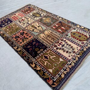 Pu&ograve; includere: Un tappeto rettangolare caratterizzato da una griglia di dodici pannelli distinti, ognuno con motivi geometrici e floreali unici nei toni del blu navy, verde oliva, crema, marrone e rosa, rifinito con un bordo blu scuro e frange.