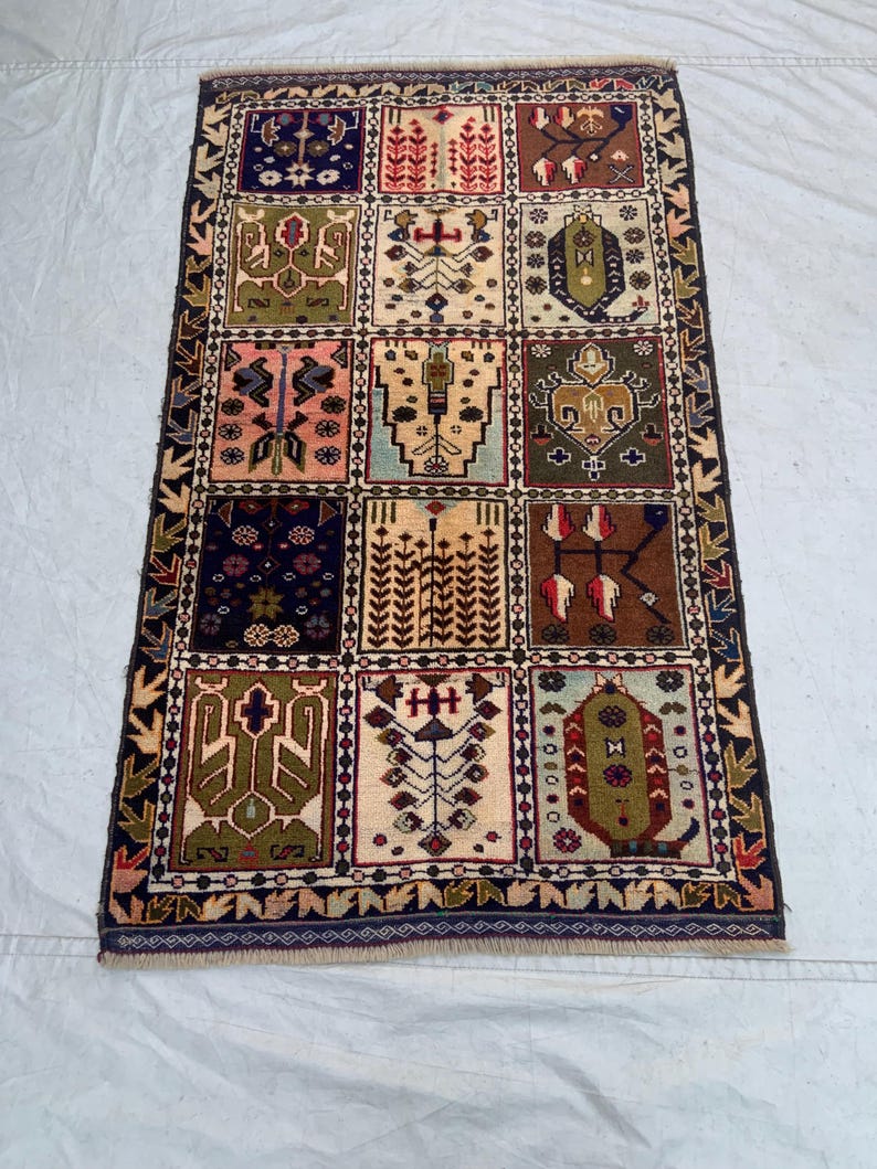 Pu&ograve; includere: Un tappeto rettangolare caratterizzato da una griglia di dodici pannelli distinti, ognuno dei quali mostra motivi geometrici e floreali unici nei toni del blu navy, verde oliva, terracotta, rosa e crema, racchiusi da un bordo scuro decorato.