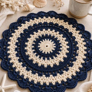 May include: A circular crochet doily featuring alternating concentric rings of navy blue and cream yarn. The design includes a central starburst pattern, intricate geometric stitches, and a scalloped edge finished with navy blue shell motifs.