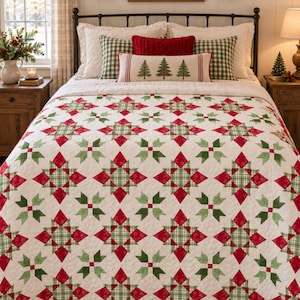 May include: A bed quilt featuring a repeating star pattern in red and green on a white background. The quilt is layered over a bed with white pillows, green and white checkered pillows, a red textured pillow, and a long lumbar pillow with trees.