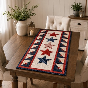 May include: A rectangular table runner with a patriotic theme. The runner features red, white, and blue colors with star and stripe designs. The runner is placed on a wooden table, with two upholstered chairs on either side.