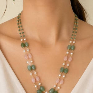 May include: A double-strand necklace and matching drop earrings featuring oval-shaped green and light pink beads interspersed with small white pearls on a gold-toned chain. The jewelry set displays a symmetrical arrangement of colored stones and pearls.