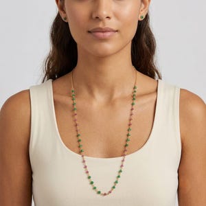 May include: A long gold chain necklace featuring alternating small green and pink gemstone beads spaced evenly along the length. The necklace is worn with matching small green stud earrings, each featuring a single round green gemstone.