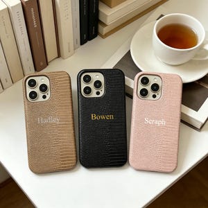 Può includere: Tre cover per smartphone con una texture a pelle di coccodrillo nei colori marrone chiaro, nero e rosa tenue. Ogni cover presenta un ritaglio per la fotocamera e un nome personalizzato stampato al centro: Hadley sulla marrone, Bowen sulla nera e Seraph sulla rosa.