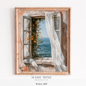 May include: A framed wall art print depicting an open window overlooking the sea. A citrus tree with orange fruit grows beside the window frame, which is draped with sheer white curtains. The scene features a stone ledge and blue ocean water.