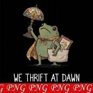 May include: A green frog illustration wearing a patterned orange cape, holding a stained glass lamp in one hand and carrying a white tote bag containing a framed picture in the other, with the text WE THRIFT AT DAWN printed below the graphic.
