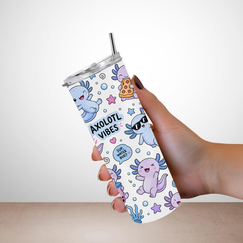 Peut inclure: Un gobelet cylindrique blanc avec un couvercle transparent et une paille en m&eacute;tal, orn&eacute; d'un motif r&eacute;p&eacute;titif d'axolotls bleu et violet clair, d'&eacute;toiles roses et de bulles. Le texte AXOLOTL VIBES et SUP, WATER BUD? est imprim&eacute; en noir.