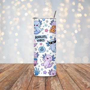 Peut inclure: Un gobelet cylindrique blanc avec une paille en m&eacute;tal, orn&eacute; d'un motif r&eacute;p&eacute;titif d'axolotls de dessin anim&eacute; dans des tons bleu et violet. Le design inclut le texte AXOLOTL VIBES et une bulle avec le texte SUP, WATER BUD? parmi des bulles et &eacute;toiles.