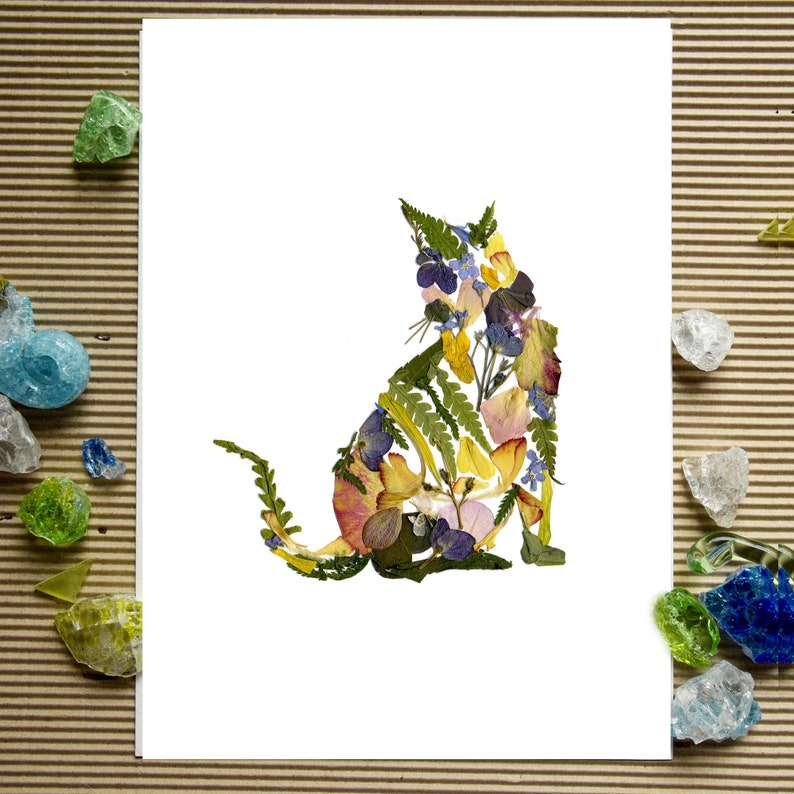 Puede incluir: Una tarjeta blanca con una silueta de gato floral hecha con flores prensadas. El gato est&aacute; sentado con la cola enroscada alrededor de su cuerpo. Las flores son de color amarillo, rosa, azul y verde.