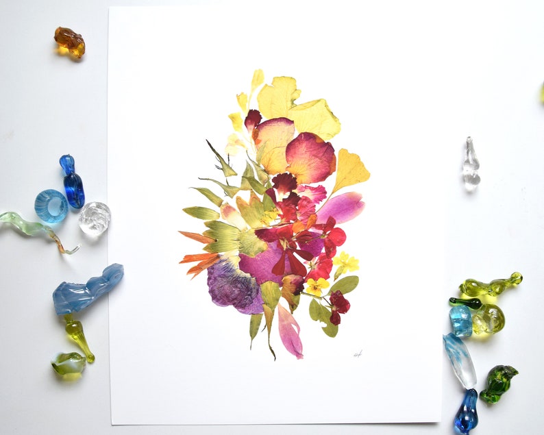 A white background with a bouquet of pressed flowers in shades of yellow, pink, red, purple, and green. The flowers are arranged in a loose, organic shape.