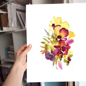 A pressed flower art print with a white background. The print features a bouquet of yellow, purple, red, and pink flowers. The flowers are arranged in a loose, organic shape. The print is signed in the bottom right corner.