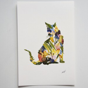 Puede incluir: Una silueta de gato colorida hecha con flores y hojas prensadas. El gato est&aacute; sentado con la cola enroscada alrededor de su cuerpo. Las flores son en tonos de amarillo, naranja, rosa, azul y verde.