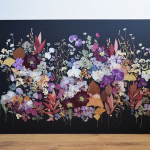 K&ouml;nnte beinhalten: Ein rechteckiges Wandkunstwerk mit einer dichten Anordnung aus gepressten, getrockneten Blumen und Bl&auml;ttern in Violett-, Rosa-, Wei&szlig;-, Gelb- und Braunt&ouml;nen vor einem einfarbigen schwarzen Hintergrund, das eine lebendige botanische Darstellung bildet.