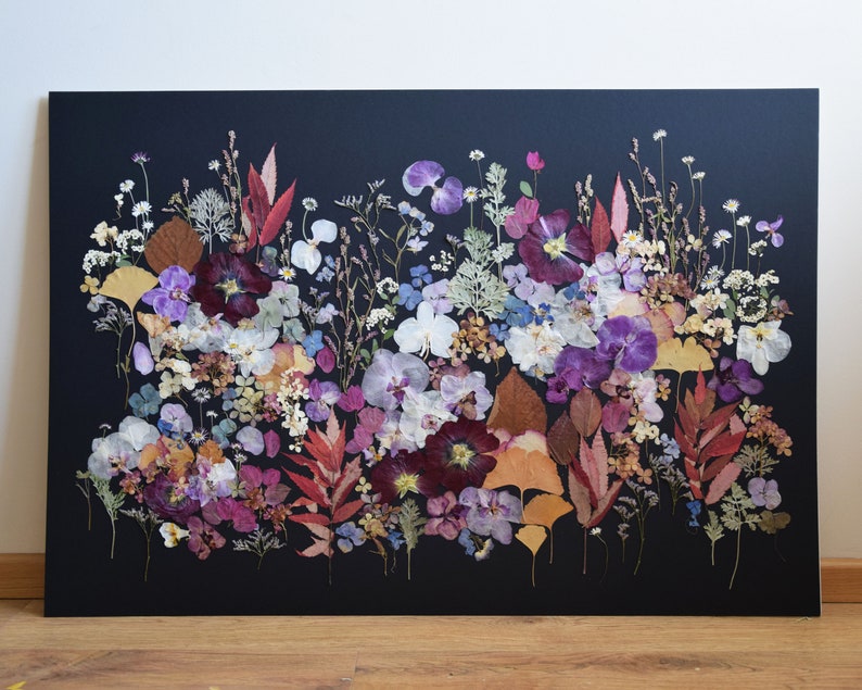 K&ouml;nnte beinhalten: Ein rechteckiges Wandkunstwerk mit einer dichten Anordnung aus gepressten, getrockneten Blumen und Bl&auml;ttern in Violett-, Rosa-, Wei&szlig;-, Gelb- und Braunt&ouml;nen vor einem einfarbigen schwarzen Hintergrund, das eine lebendige botanische Darstellung bildet.