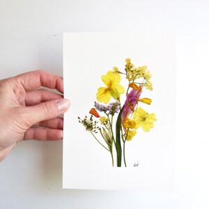 Puede incluir: Una impresi&oacute;n de arte de flores prensadas con un ramo de flores amarillas, naranjas y moradas sobre un fondo blanco. La impresi&oacute;n est&aacute; firmada "heft".