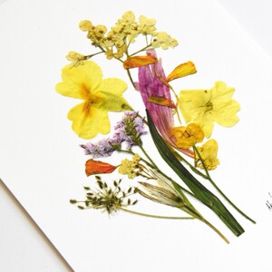 Puede incluir: Una obra de arte de flores prensadas que presenta un ramo de flores amarillas, naranjas, rosas y blancas sobre un fondo blanco. Las flores est&aacute;n dispuestas en un estilo suelto y natural. La pieza est&aacute; firmada "hart" en la esquina inferior derecha.