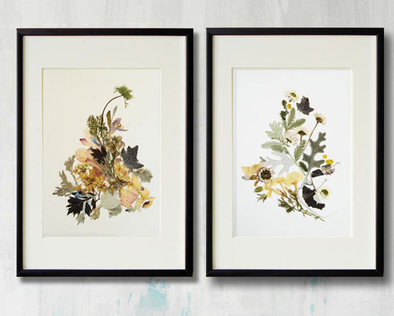 May include: Two framed botanical prints featuring pressed flowers and leaves. The print on the left features a bouquet of yellow, pink, and green flowers and leaves. The print on the right features a bouquet of white and green flowers and leaves.