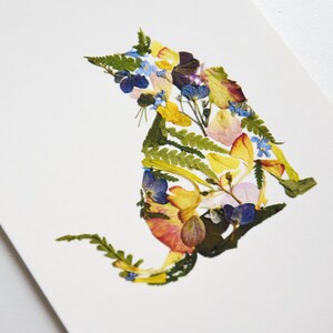 Puede incluir: Una silueta de gato colorida hecha de flores y hojas prensadas. El gato es amarillo, rosa, azul y verde.