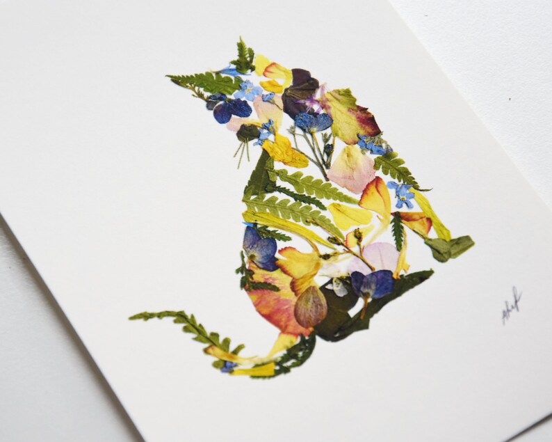 Puede incluir: Una silueta de gato colorida hecha de flores y hojas prensadas. El gato es amarillo, rosa, azul y verde.