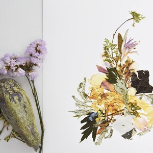 May include: A pressed flower arrangement with a variety of dried flowers and leaves in shades of yellow, green, and purple. The flowers are arranged in a loose, organic style, and the overall effect is one of natural beauty.