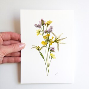 Puede incluir: Una impresi&oacute;n de arte de flores prensadas con un ramo de flores silvestres amarillas y moradas sobre un fondo blanco. La impresi&oacute;n est&aacute; firmada "M.H."