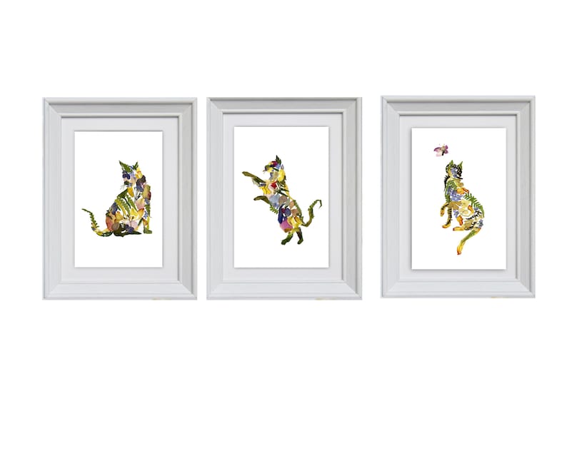 Puede incluir: Tres marcos de fotos blancos con un dise&ntilde;o de gato floral en cada uno. El gato del marco de la izquierda est&aacute; sentado, el gato del marco del medio est&aacute; saltando y el gato del marco de la derecha est&aacute; mirando hacia arriba a una mariposa.