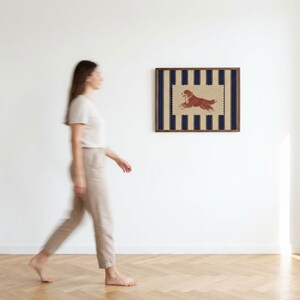 Puede incluir: Una pieza de arte mural rectangular enmarcada que presenta un panel central de color tostado con un borde festoneado. El panel muestra una ilustraci&oacute;n marr&oacute;n de un perro en posici&oacute;n de correr, sobre un fondo de rayas verticales azul marino y tostado.